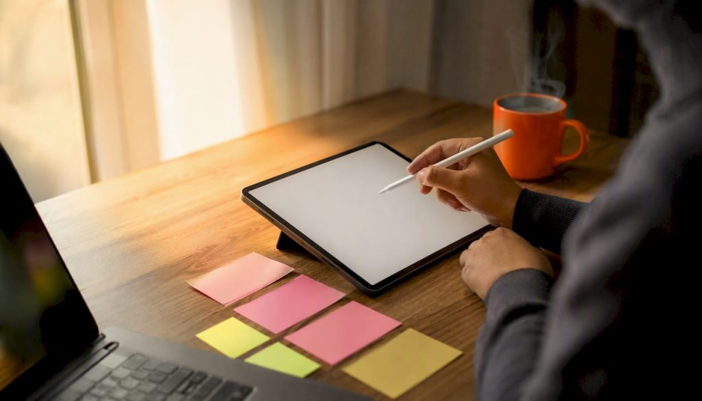 Hands using stylus over digital tablet with sticky notes