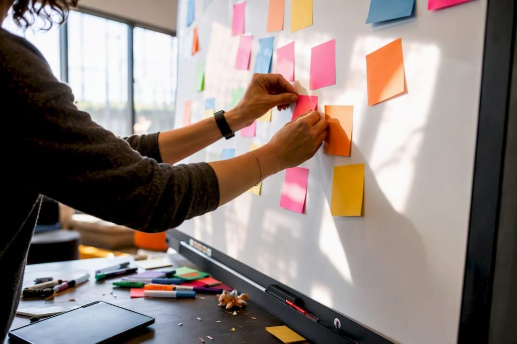 Hands arranging sticky notes on whiteboard